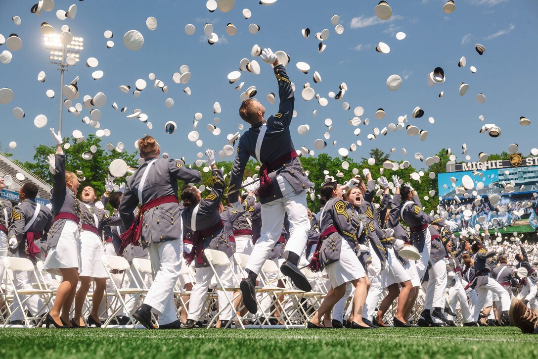 U.S. Military Academy cadets toss their caps in the air on a football field.