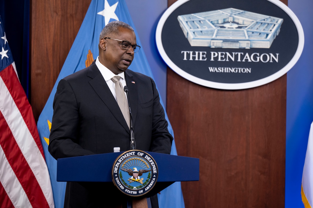 A man standing at a lectern answers question. A sign behind him indicates that he is at the Pentagon.
