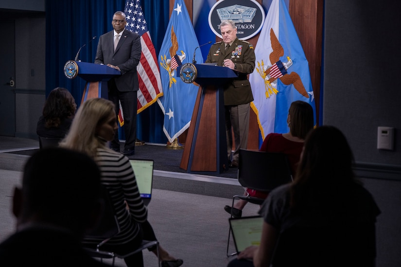 A civilian and soldier brief members of the media. The sign behind them indicates that they are at the Pentagon.