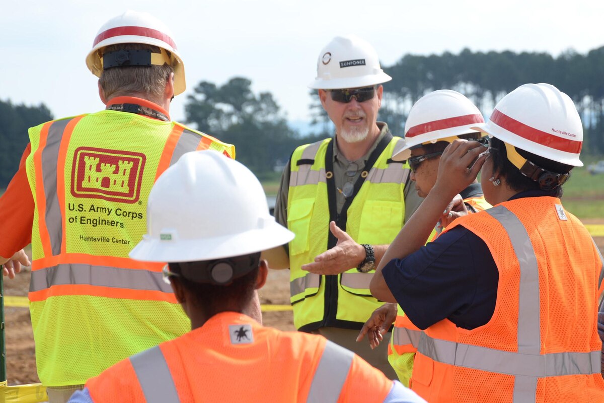 Four people wearing orange and yellow vests receive a site brief from another person.