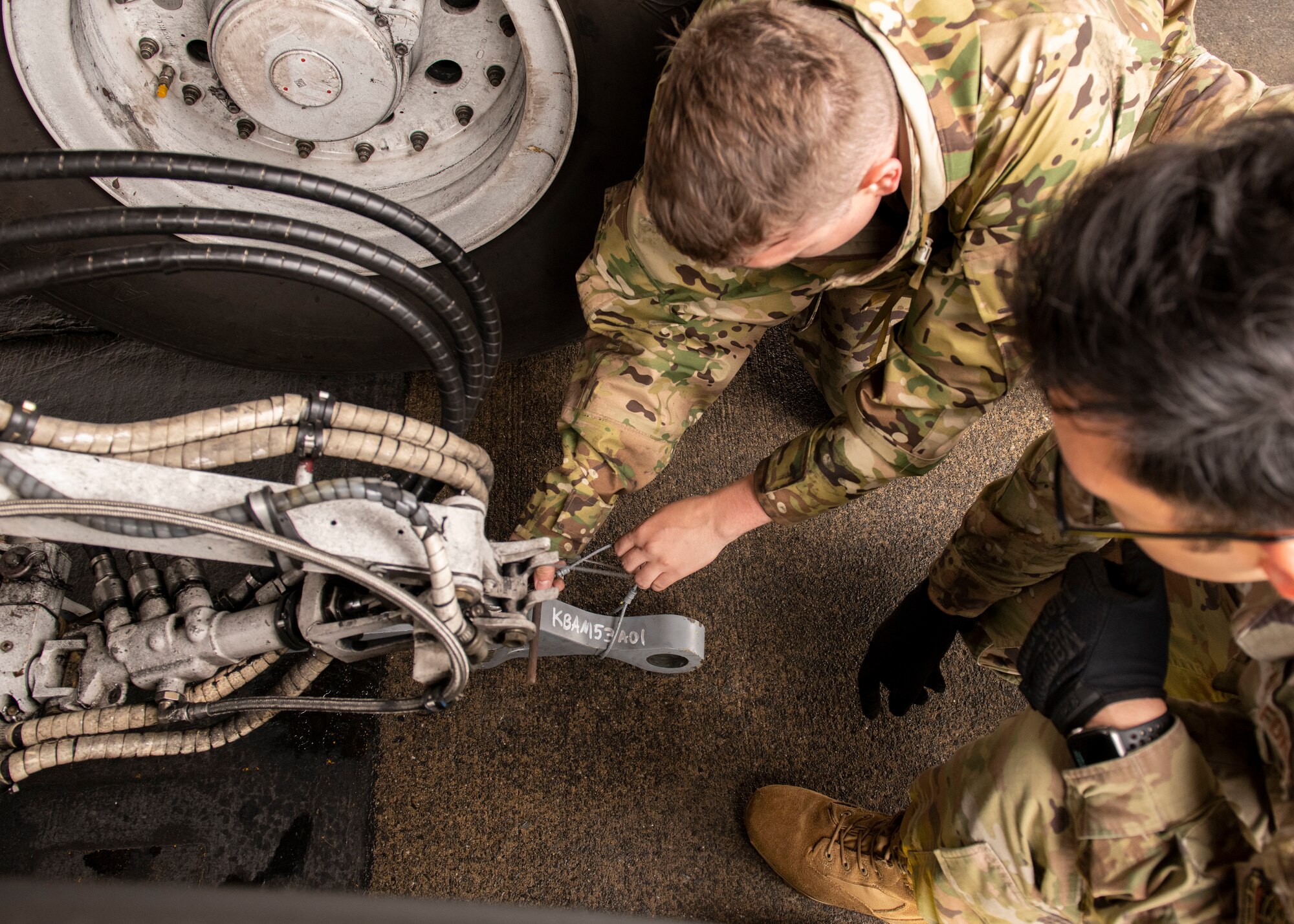 A top-down view of two airmen attaching a tow bar to an airplane's landing gear