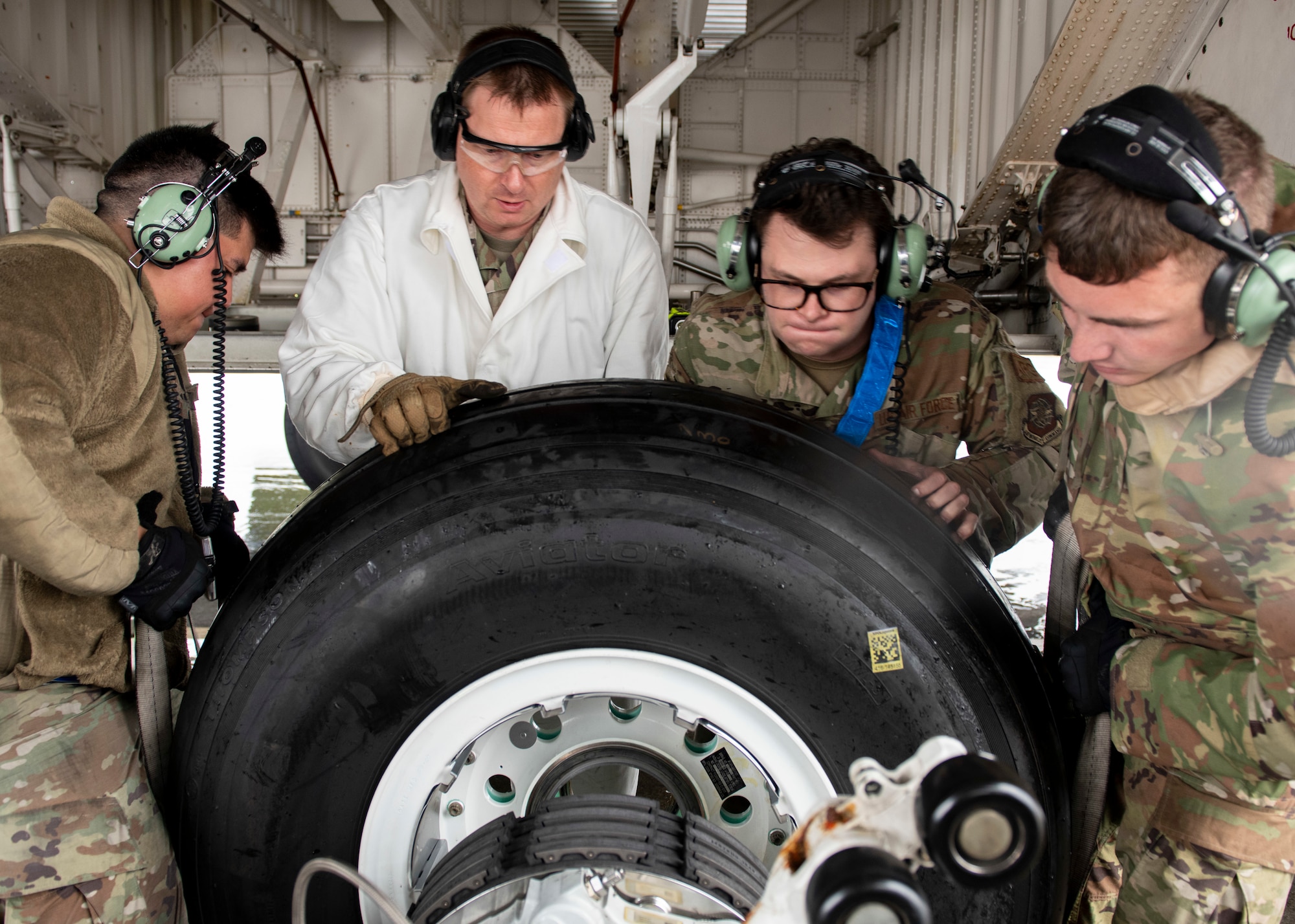 Four airmen in hoist a airplane tire off its hub