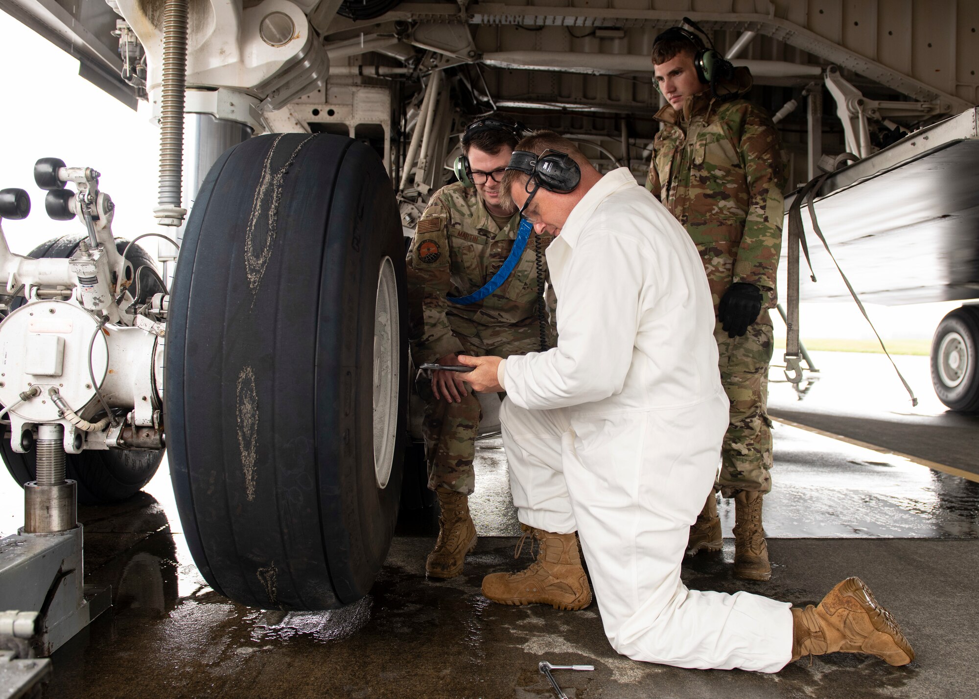 An airman helps a mechanic in a white smock fix a airplane tire