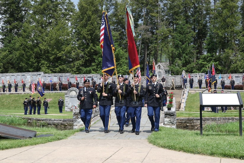 Soldiers of the 28th Infantry Division march the unit's colors over a footbridge at the conclusion of the annual memorial service May 22, 2022. Immediately behind the color guard and directing the march is Command Sgt. Maj. Randall Pritts, the division command sergeant major. The division shrine is located to the rear of the bridge.