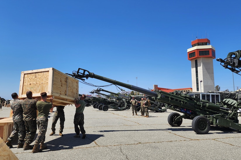 Several service members lift a large wood box loaded with equipment.