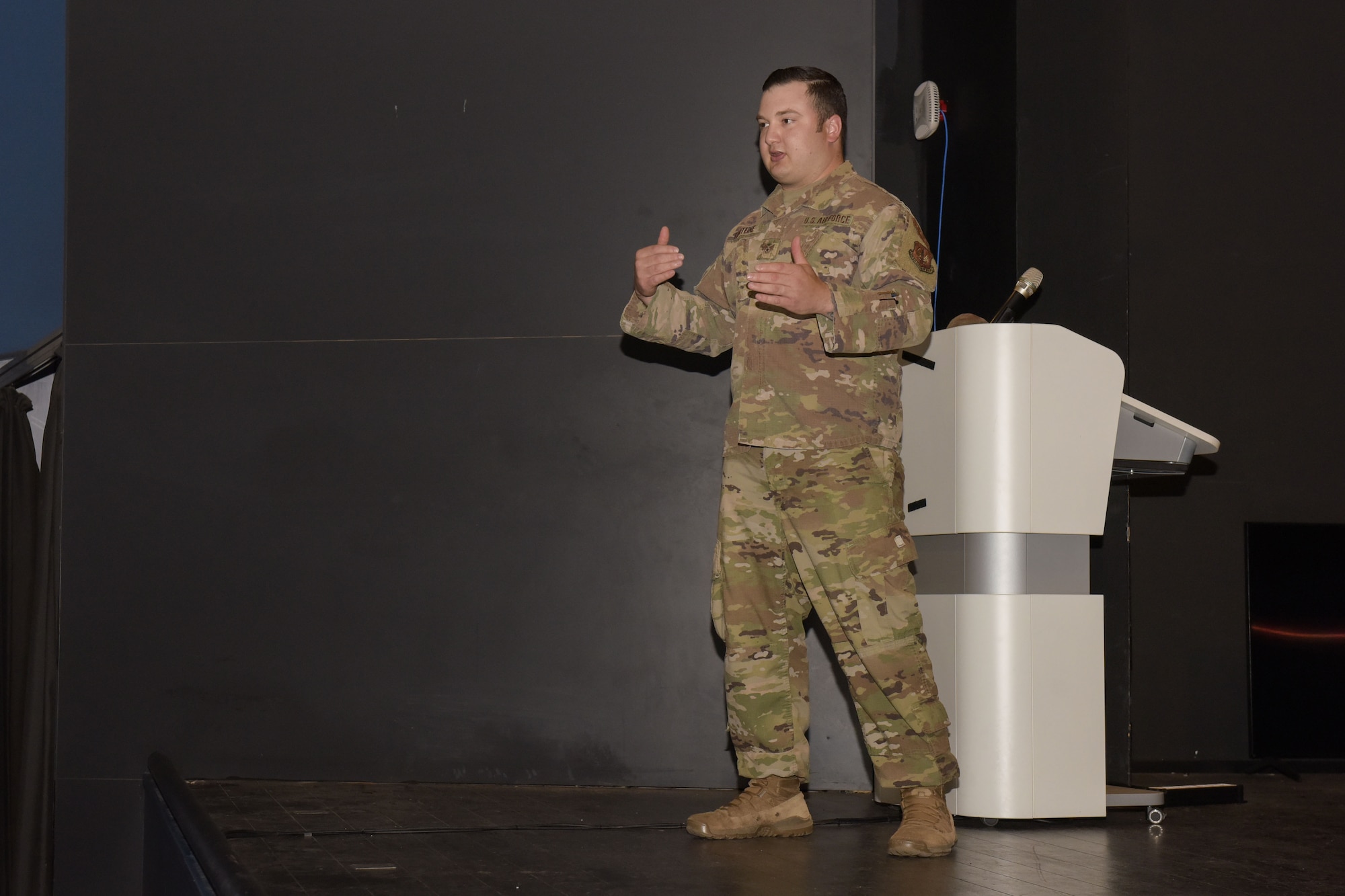 Airman stands on stage and delivers a briefing