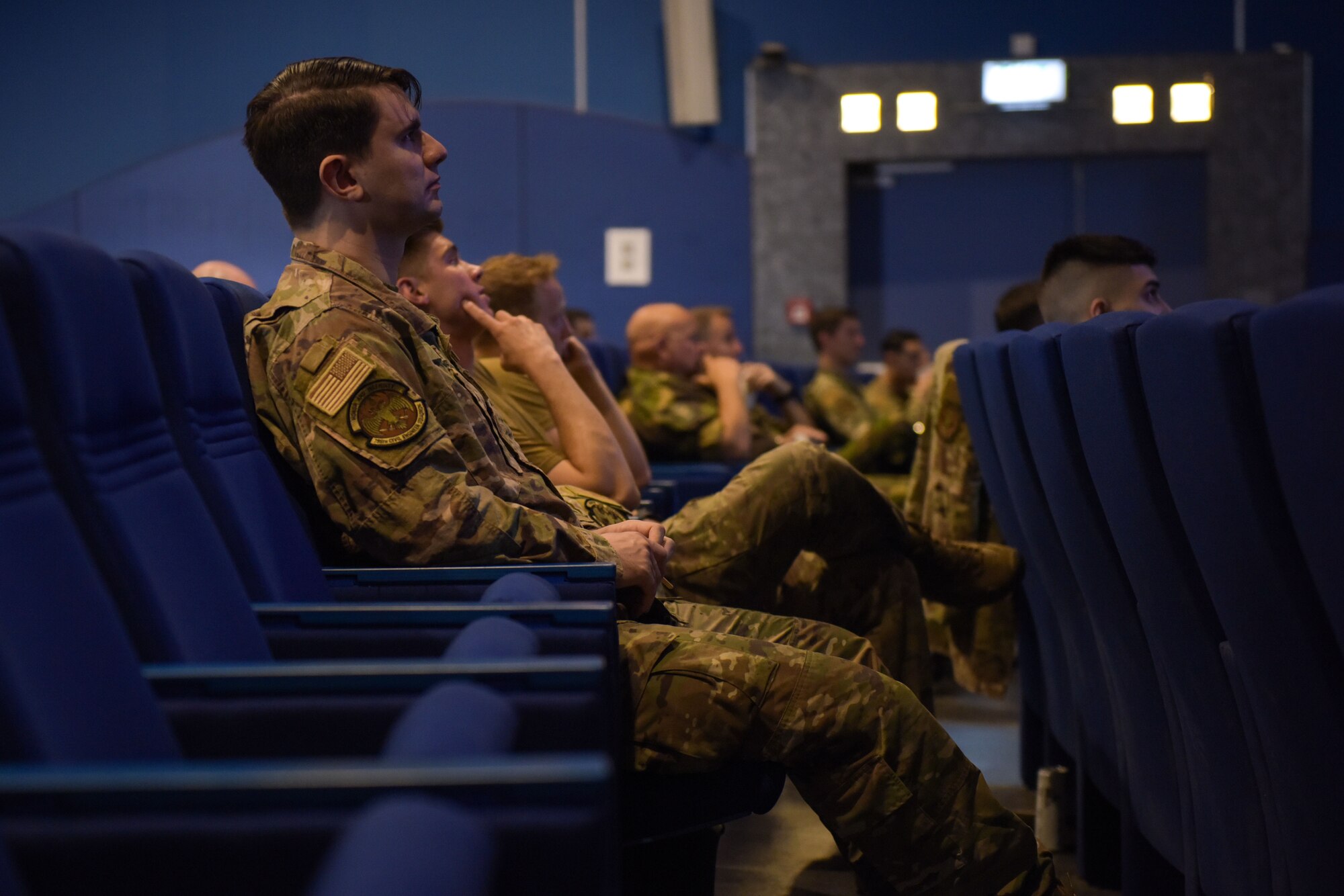 Airmen sit in chairs and watch a speaker