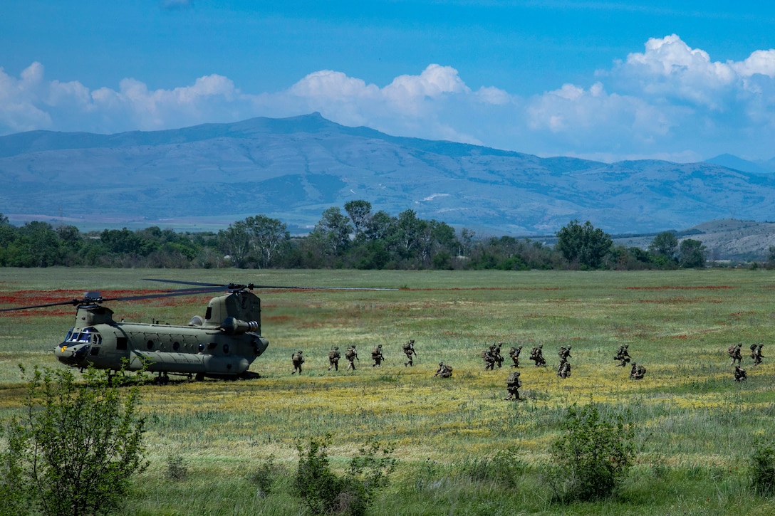Soldiers  walk across a large field away from a helicopter.