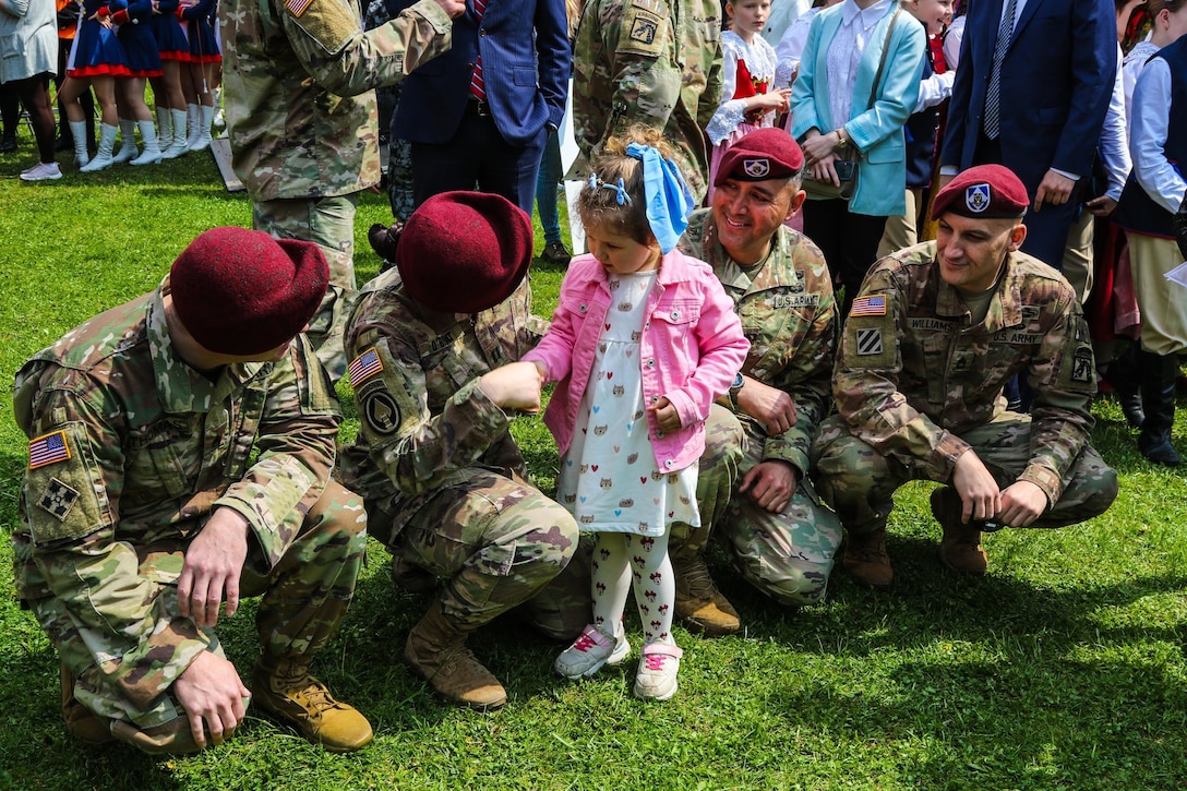 A young girl shakes hands with a soldier as others kneel close by.
