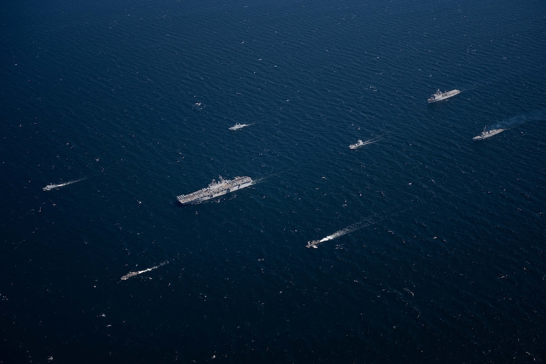Ships sail in formation in dark blue water.