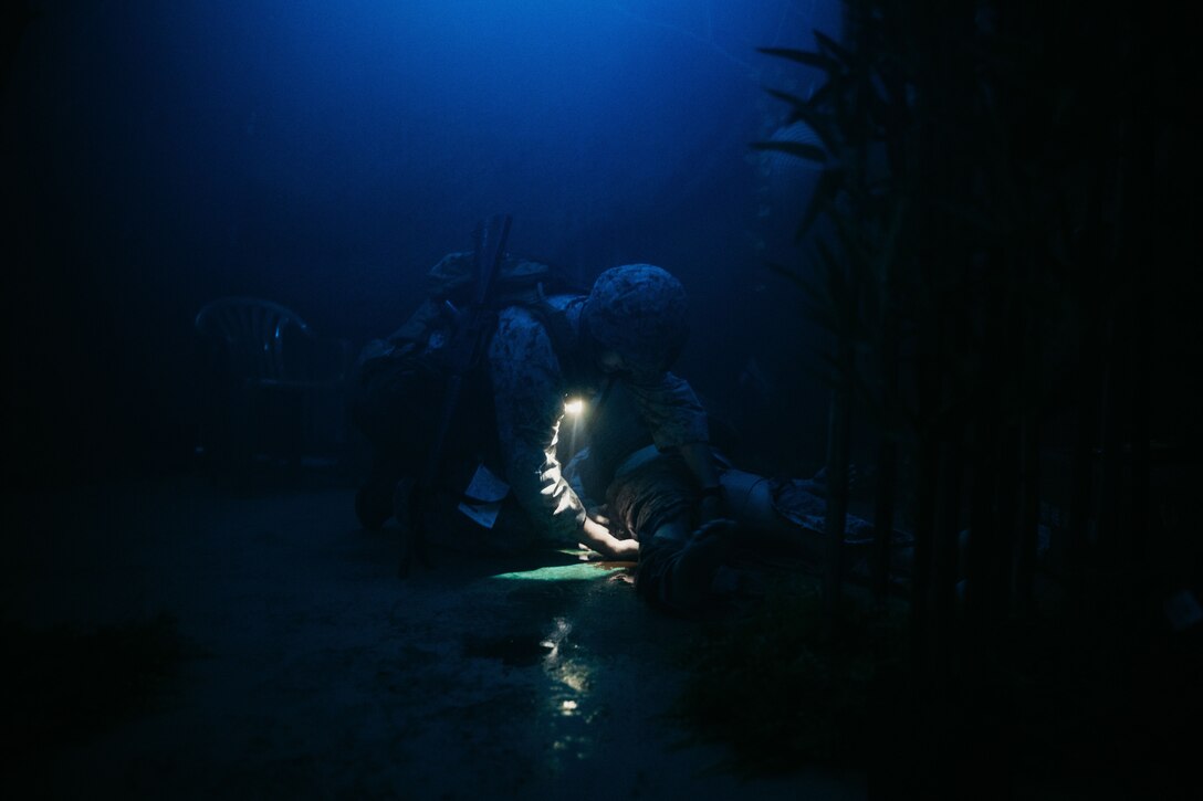 A Marine performs medical care on a mannequin in the dark during a course.