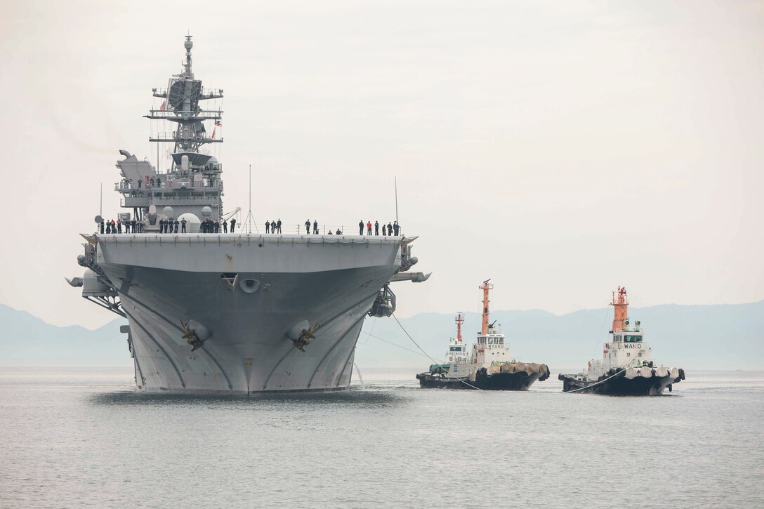 A large ship transits a body of water near two small ships connected by ropes.