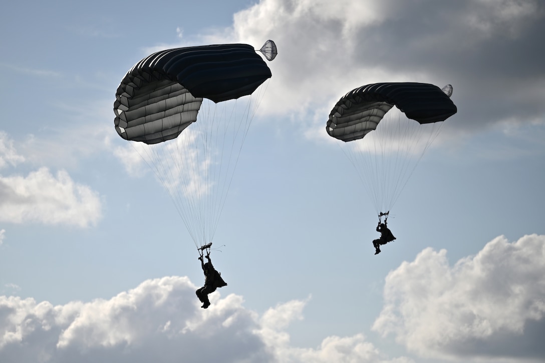 Two airmen parachute to the ground.