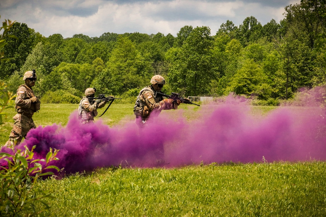 Three soldiers aim weapons in a field surrounded by clouds of purple smoke.