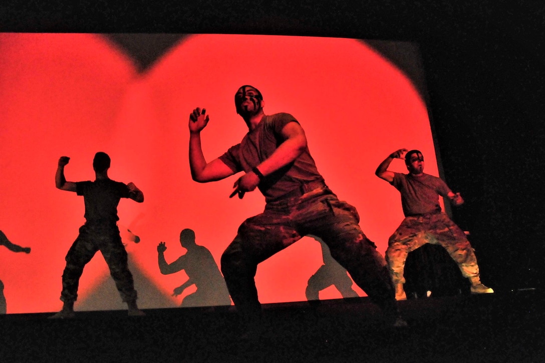 Soldiers illuminated by red light perform on stage.