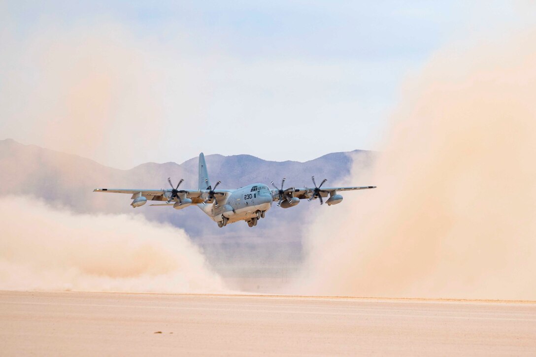 An aircraft flies low to the ground as dust surrounds it.