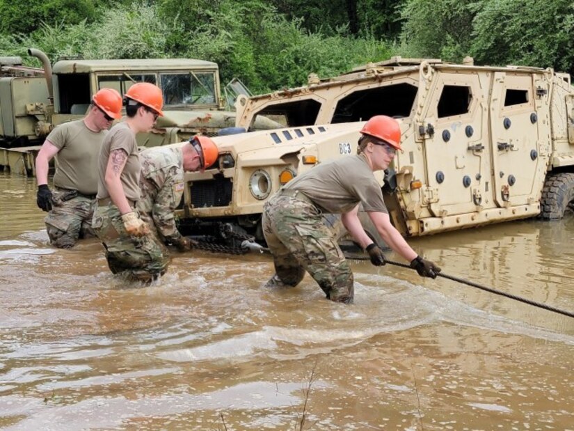 Soldiers pull a rope attached a car in standing water.