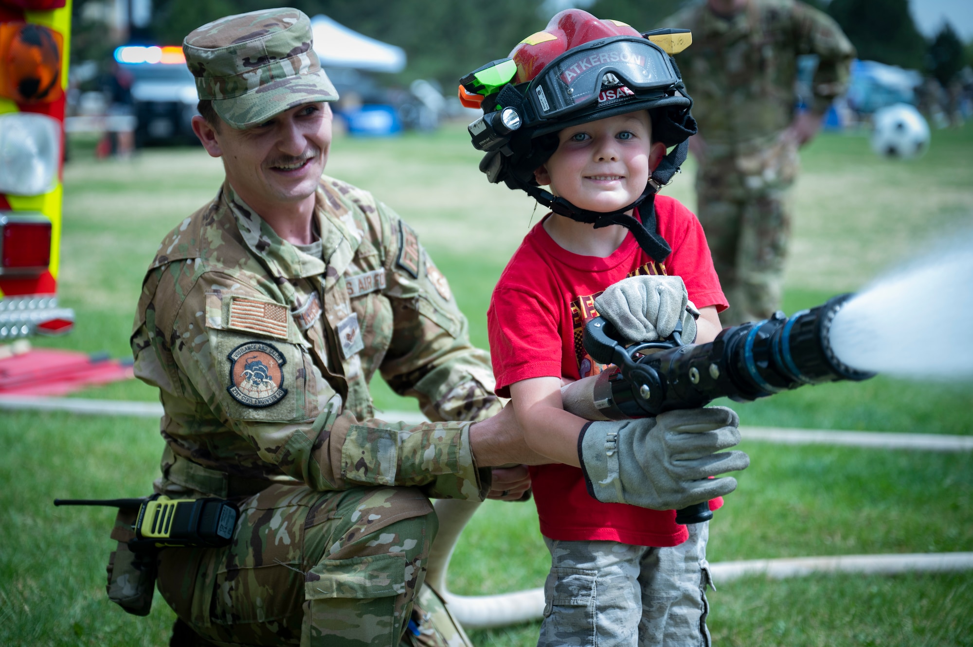 U.S. Air Force Staff Sgt. Bryce Atkerson, 21st Civil Engineer Squadron fire protection crew chief, shows Isaiah, 5, how to operate a fire hose at the Defender’s Fair at Peterson Space Force Base, Colorado, May 19, 2022. The event was hosted to celebrate Police Week, which was established when President John F. Kennedy signed a proclamation designating May 15th as Peace Officers Memorial Day and the week in which that date falls during Police Week. (U.S. Space Force photo by Senior Airman Jonathan Whitely)