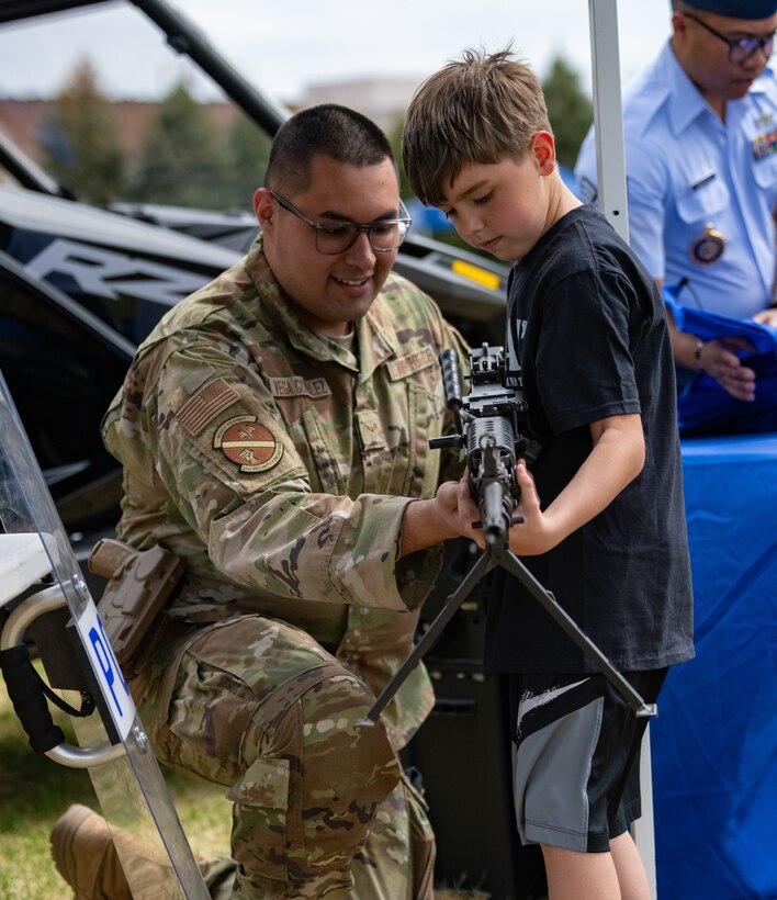 U.S. Air Force Airman 1st Class Francisco Vega Gonzalez, left, 21st Security Force Squadron armorer, shows Liam, 8, an unloaded M249 light machine gun at the Defender’s Fair, at Peterson Space Force Base, Colorado, May 19, 2022. The event, which had food trucks, games and law enforcement displays, was hosted to celebrate Police Week. (U.S. Space Force photo by Airman 1st Class Ryan Prince)