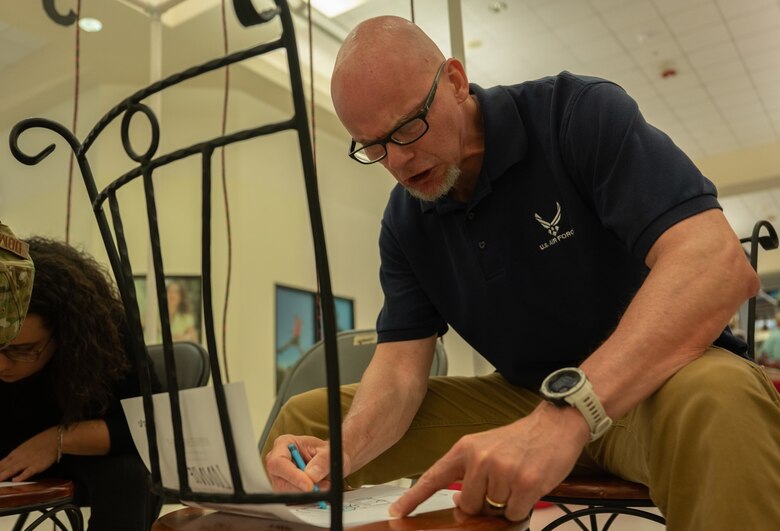 Lonnie McCarron, 21st Security Forces Squadron military and family life counselor, colors a picture while locked away in a cell made of strings at Peterson Space Force Base, Colorado, May 18, 2022. The event was hosted at the Base Exchange and raised more than $400 dollars for the Pikes Peak Peace Officer Memorial (U.S. Space Force photo by Senior Airman Jonathan Whitely)