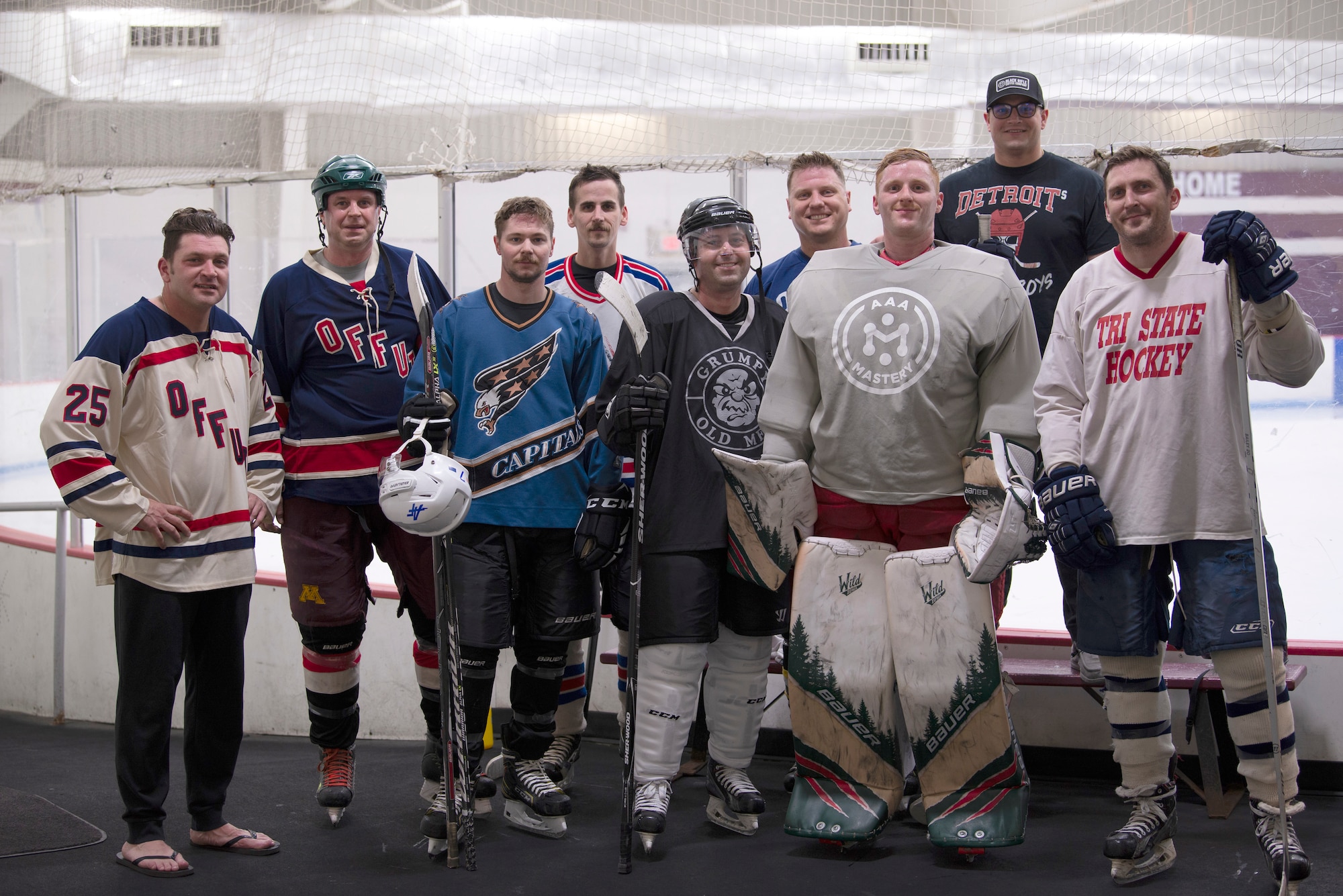 A group of hockey players pose for a photo after a practice in front of a hockey rink.