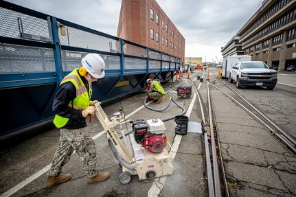 Petty Officer Second Class Brandon Kimpel, utilitiesman, (left) and Petty Officer Second Class Justin Reeves, builder, complete hazard abatement work on walkways along both sides of Farragut Avenue February 14, 2022 at Puget Sound Naval Shipyard & Intermediate Maintenance Facility in Bremerton, Washington. (U.S. Navy photo by Scott Hansen)