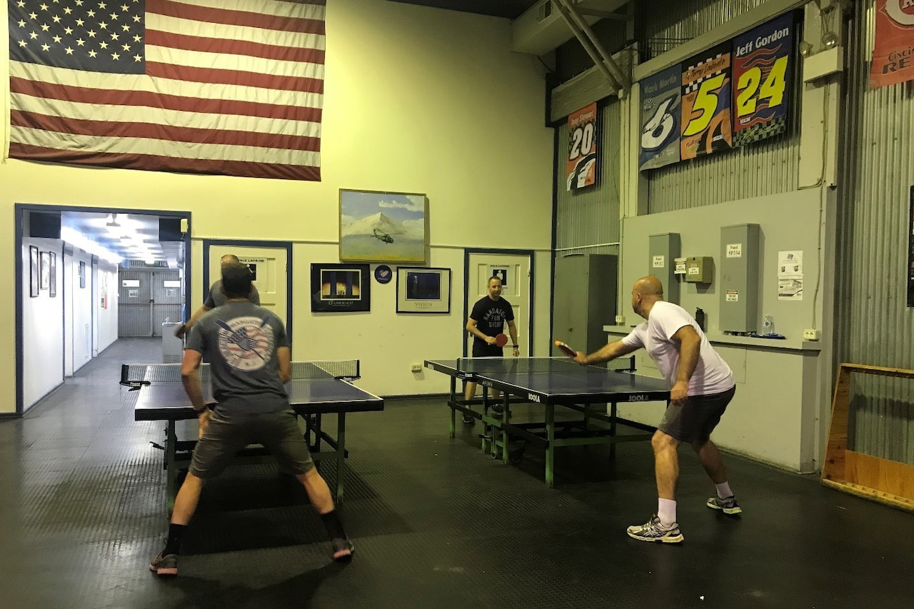 Two pairs of people play separate matches of ping pong simultaneously.