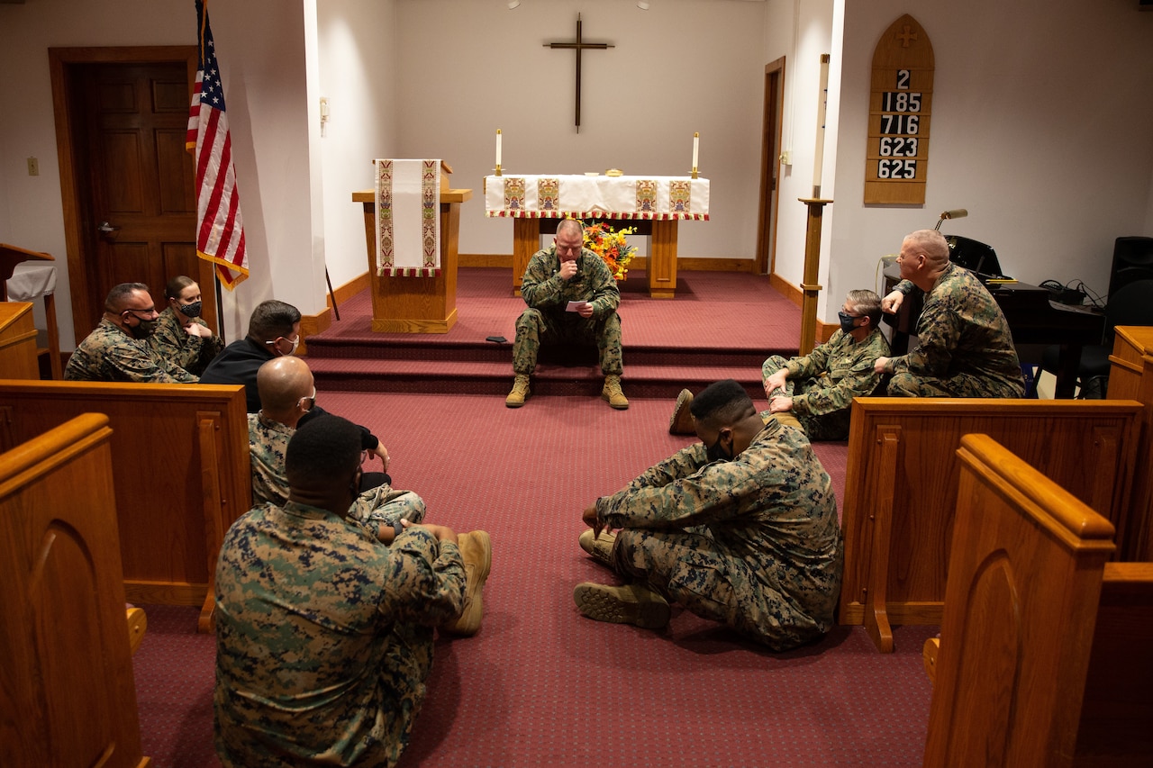 A Marine speaks to several service members inside of a church.