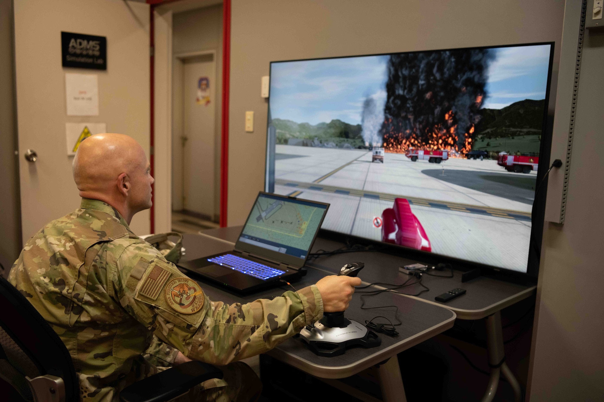 A military member sits behind a computer that trains firemen.