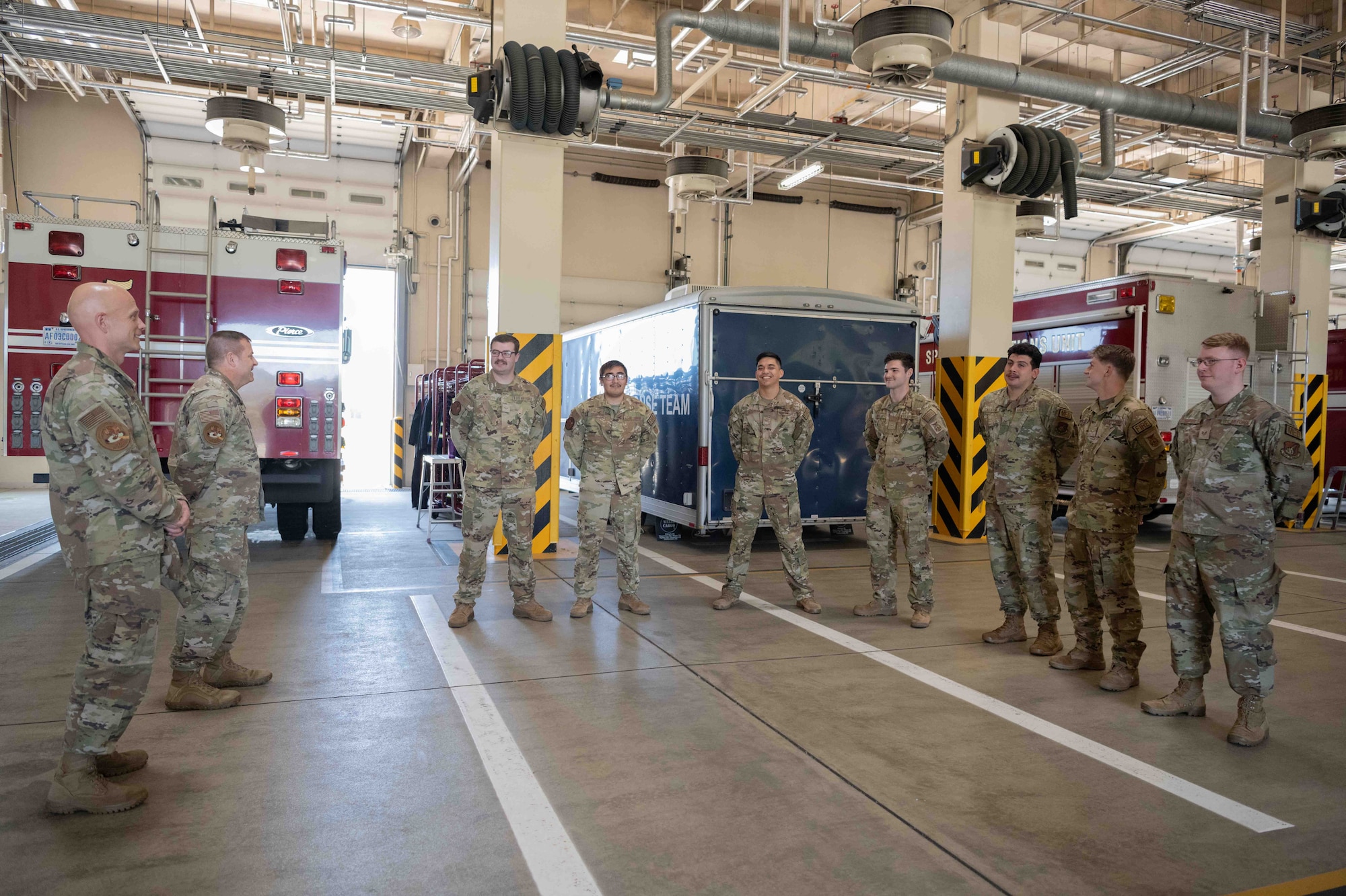 Military members talk to Airmen Firefighters in a garage.
