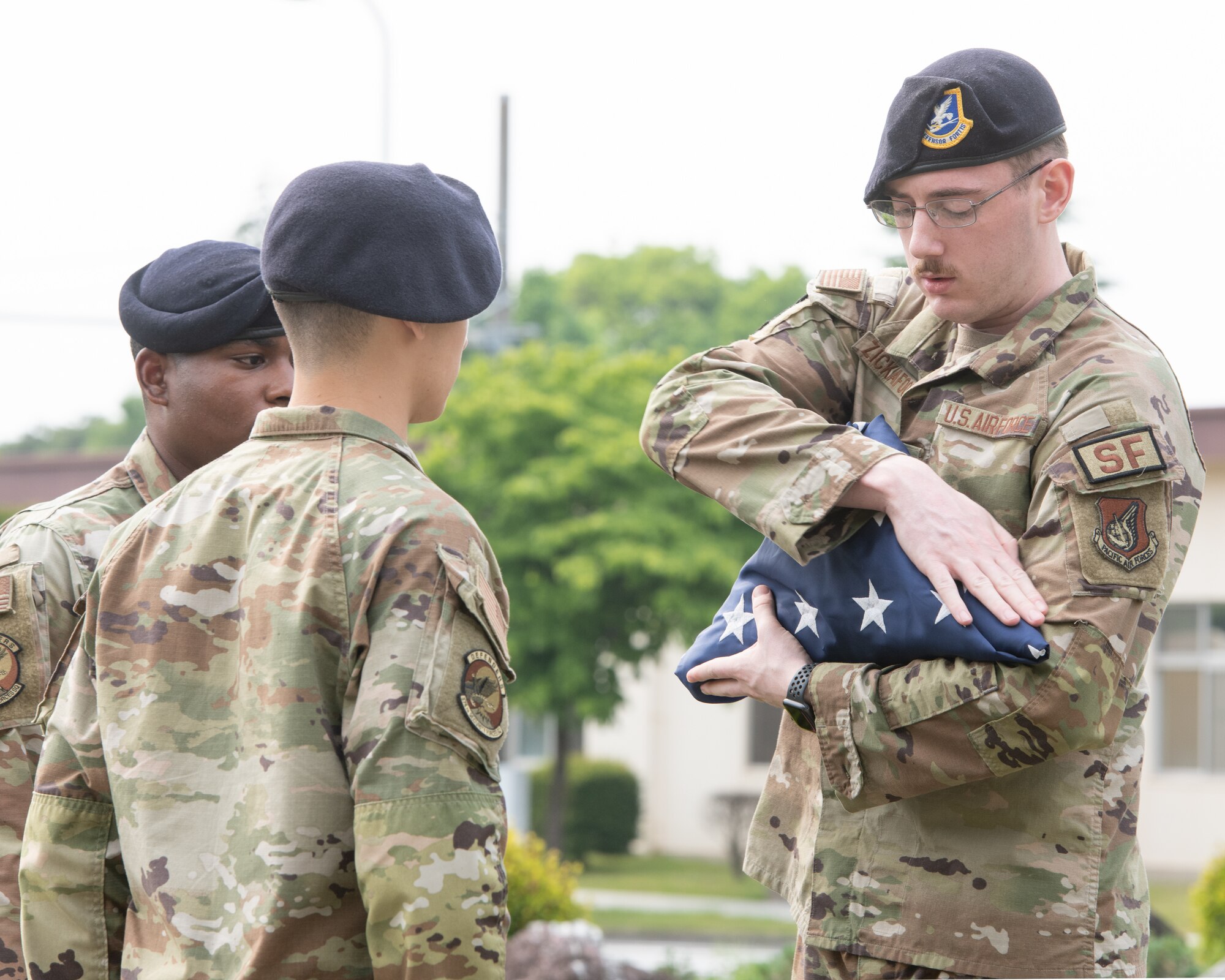 Airman 1st Class Derek Zickafoose, 374th Security Forces Squadron security response team member, dresses the American Flag during a police retreat ceremony at Yokota Air Base, Japan, May 20, 2022. The 374th SFS held the ceremony during Police Week to honor law enforcement personnel as well as recognize the dangers and risks they face every day. (U.S. Air Force photo by Machiko Arita)