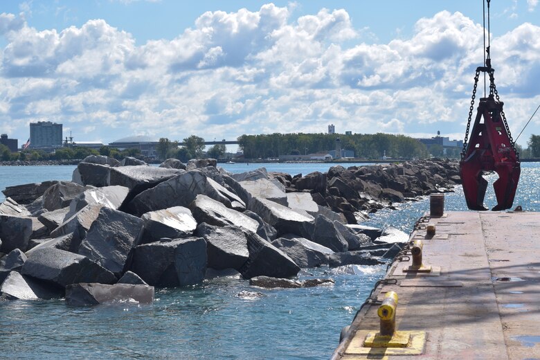 Stone breakwater next to a barge with a claw.