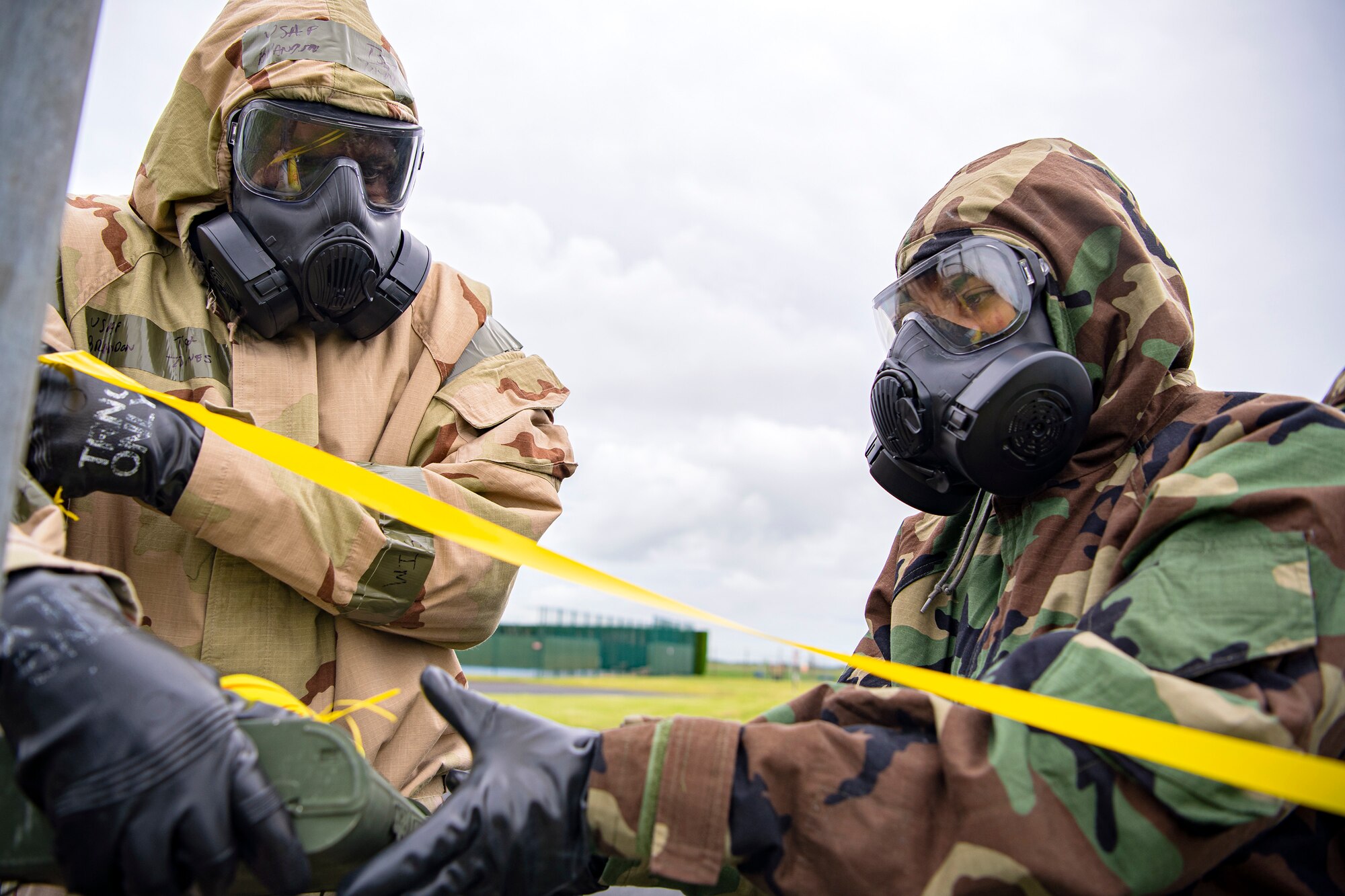 Master Sgt. Brandon Townes, left, 423d Civil Engineer Squadron section chief, holds a flagging ribbon while passing a marking sign to an Staff Sgt. Naujy Serrano, right, 423d CES emergency management NCO in charge of plans and operations, at RAF Alconbury, England, May 19, 2022. The 423d CES held an exercise designed at training Airmen on how to properly control and examine a contaminated area after a simulated chemical attack while in Mission Oriented Protective Posture Gear. (U.S. Air Force photo by Staff Sgt. Eugene Oliver)