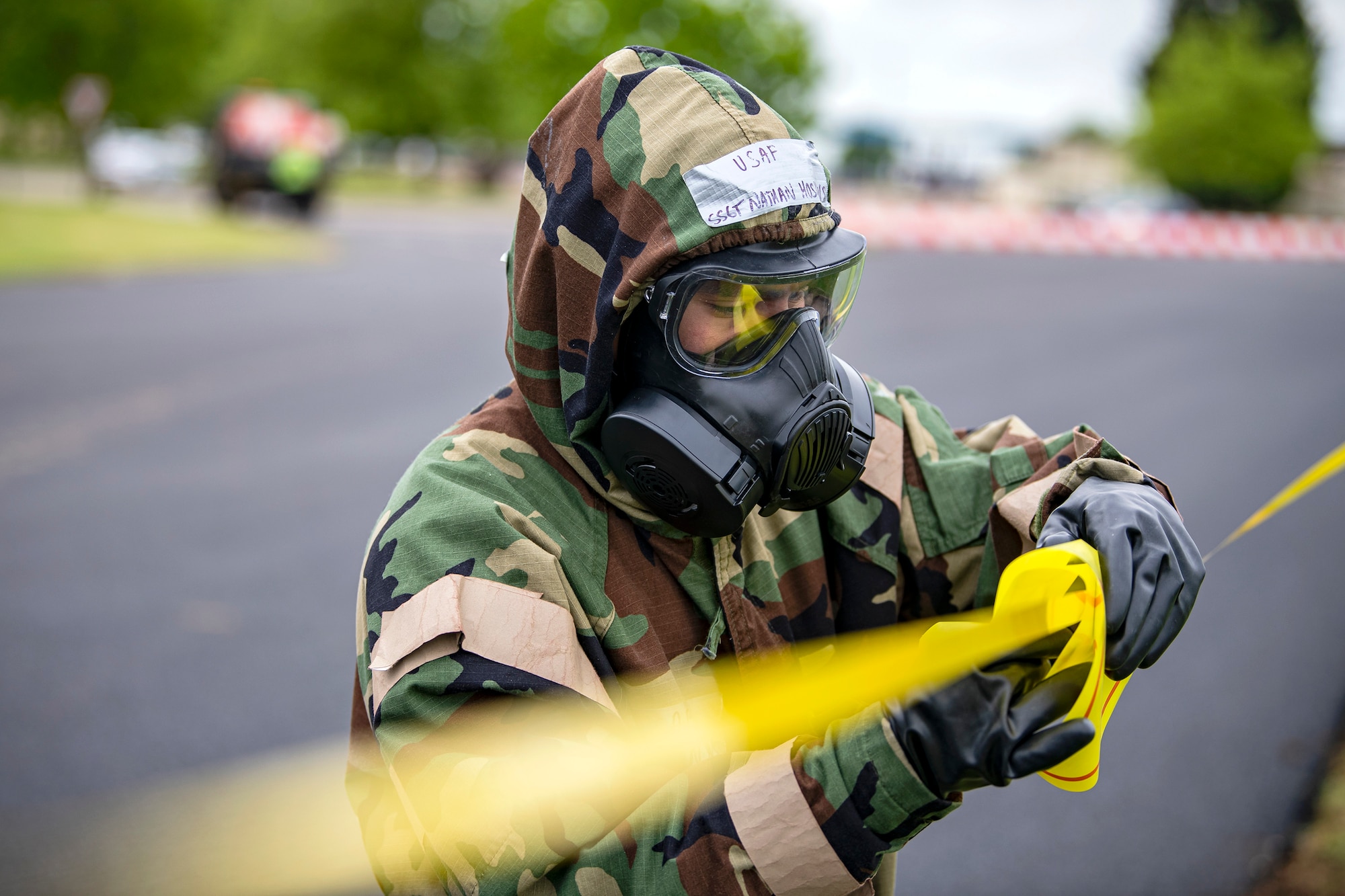 An Airman from the 423d Civil Engineer Squadron, places a marking sign on a flagging ribbon during an exercise at RAF Alconbury, England, May 19, 2022. The exercise was geared towards training Airmen on how to properly control and examine a contaminated area after a simulated chemical attack while in Mission Oriented Protective Posture Gear. (U.S. Air Force photo by Staff Sgt. Eugene Oliver)