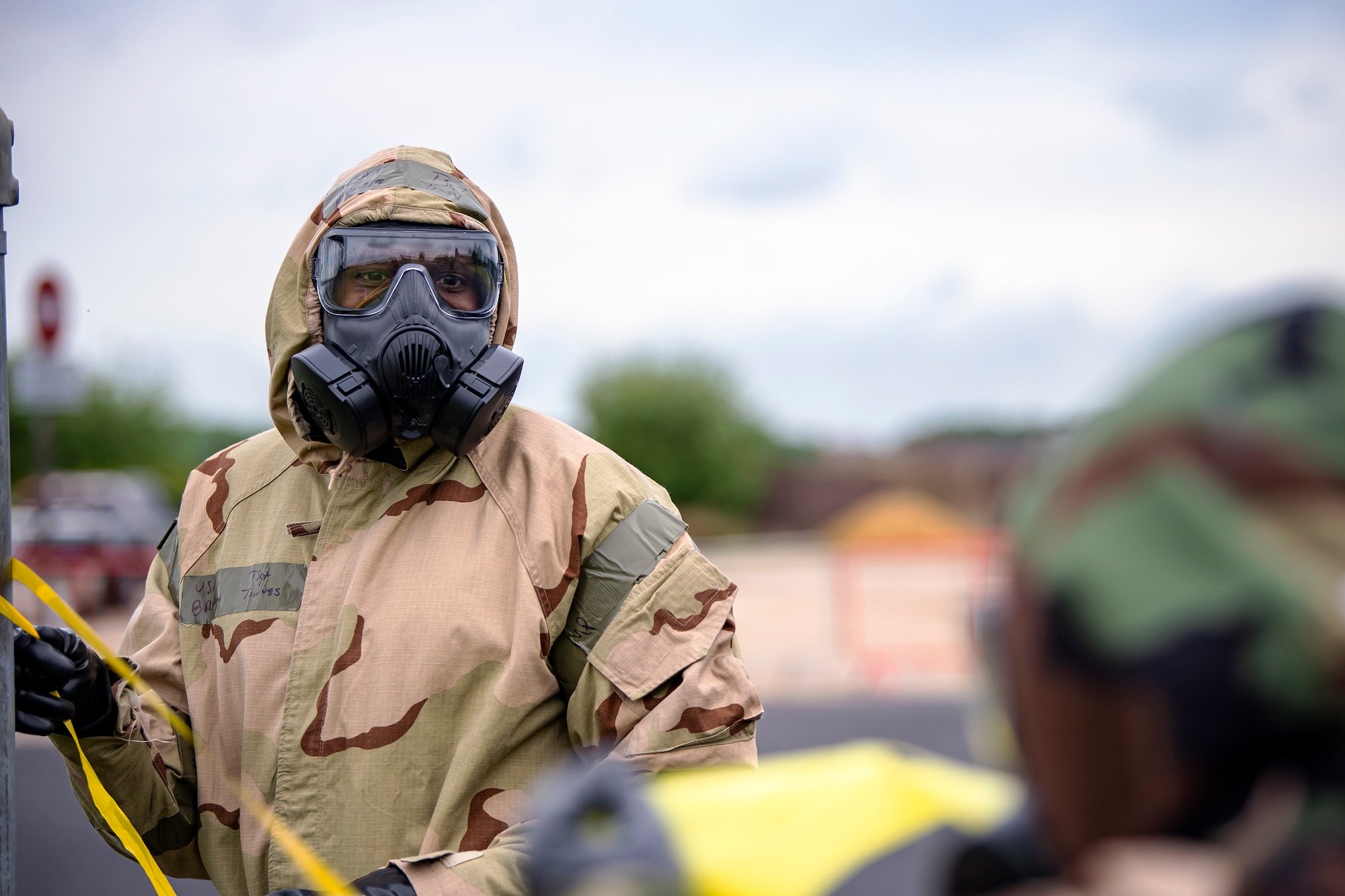 Master Sgt. Brandon Townes, left, 423d Civil Engineer Squadron section chief, holds a flagging ribbon during an Exercise at RAF Alconbury, England, May 19, 2022. The exercise was geared towards training Airmen on how to properly control and examine a contaminated area after a simulated chemical attack while in Mission Oriented Protective Posture Gear. (U.S. Air Force photo by Staff Sgt. Eugene Oliver)