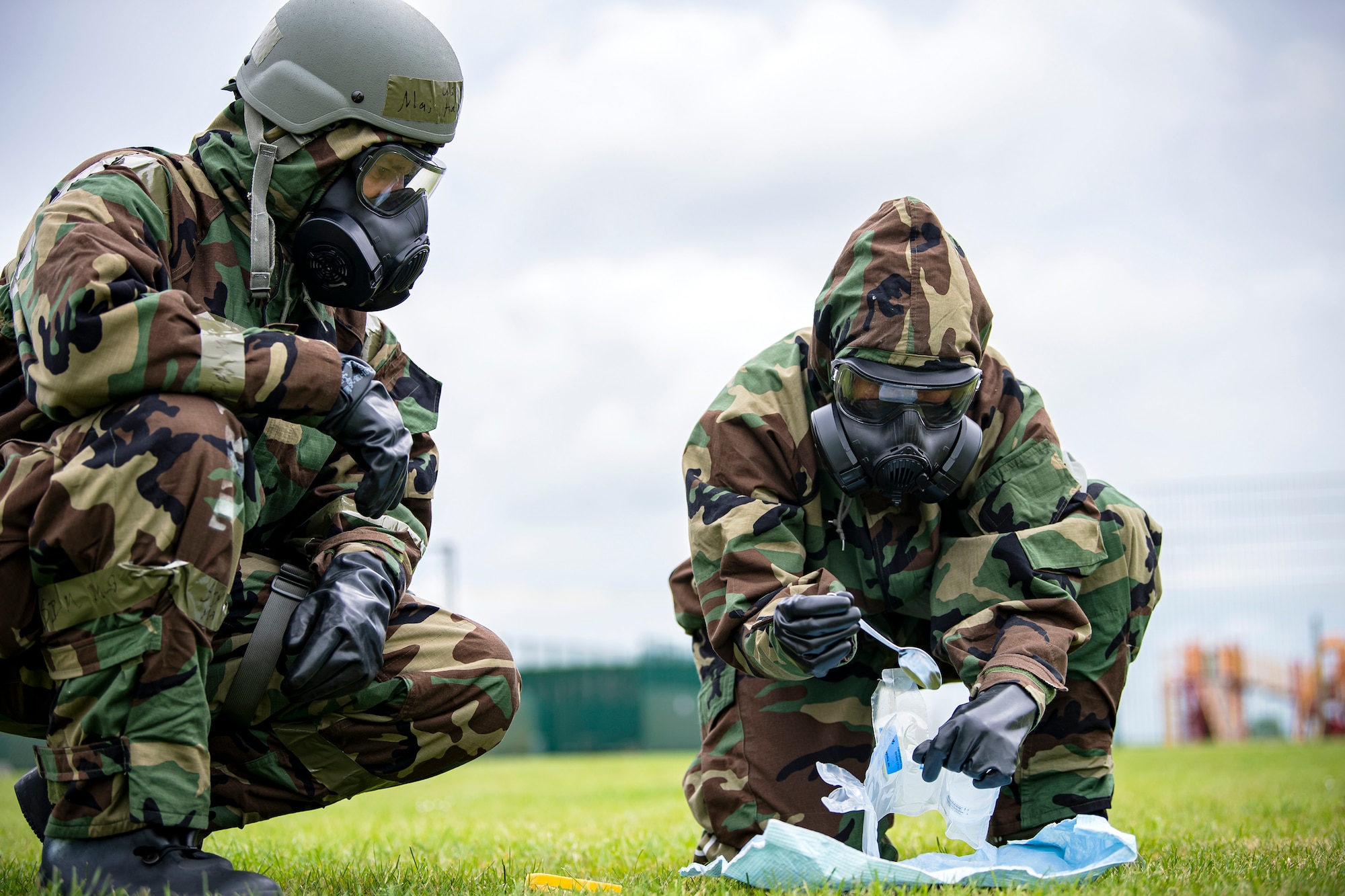 Staff Sgt. Naujy Serrano, right, 423d Civil Engineer Squadron emergency management NCO in charge of plans and operations, prepares to collect a soil sample from a simulated contaminated area during an exercise at RAF Alconbury, England, May 19, 2022. The exercise was geared towards training Airmen on how to properly control and examine a contaminated area after a simulated chemical attack while in Mission Oriented Protective Posture Gear. (U.S. Air Force photo by Staff Sgt. Eugene Oliver)