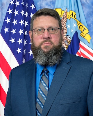 Official portrait of Heath Buswell DLA Disposition Services Mid-America with flags in the background.