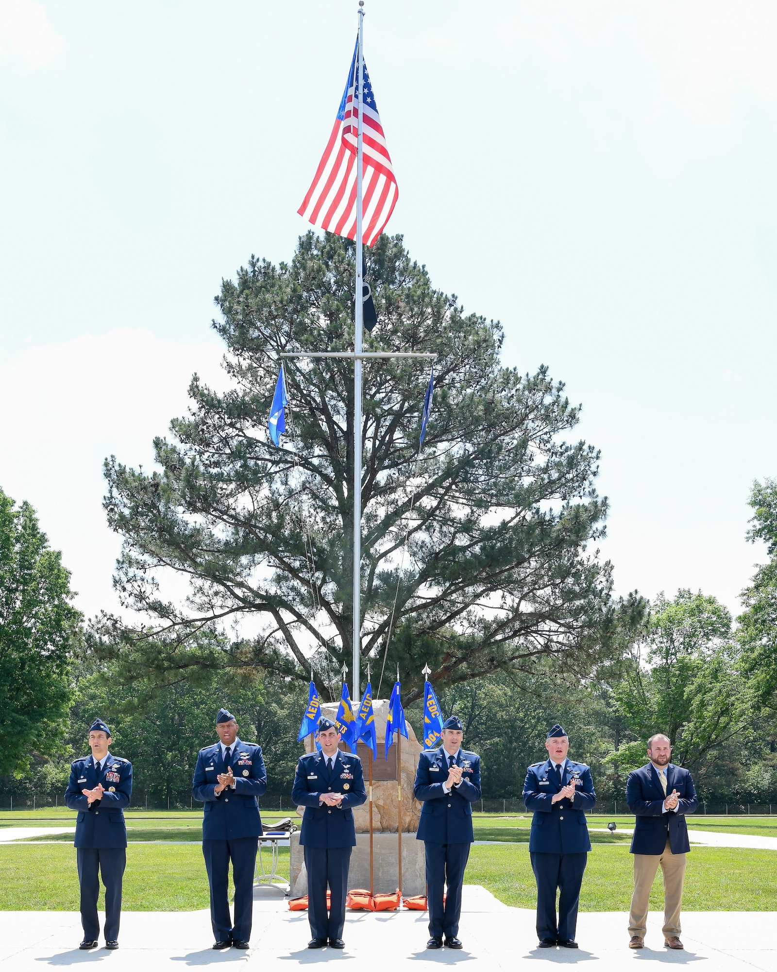 Five uniformed Airman and one civilian standing in a line clap as they sing the Air Force song