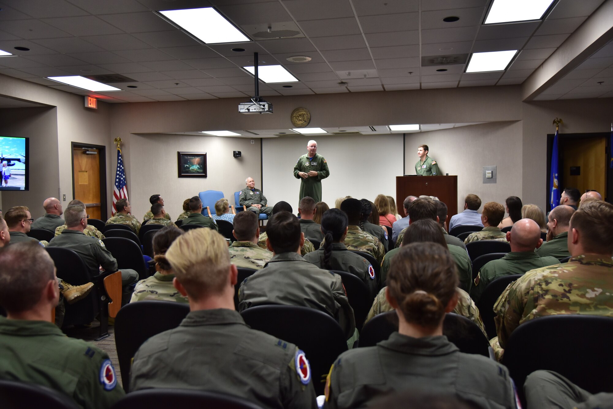 Col. Jeff Van Dootingh stands in front of a room full of people talking about the retiree, Lt. Col. Dwayne Russell, seated on the left side of the stage.