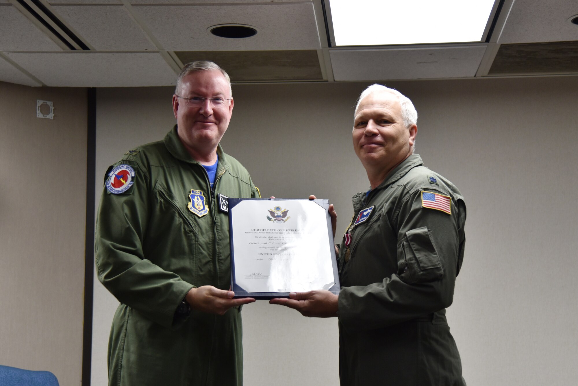 Col. Jeff Van Dootingh on left and Lt. Col. Dwayne Russell on right posing for a photo holding Russell's retirement certificate between them.