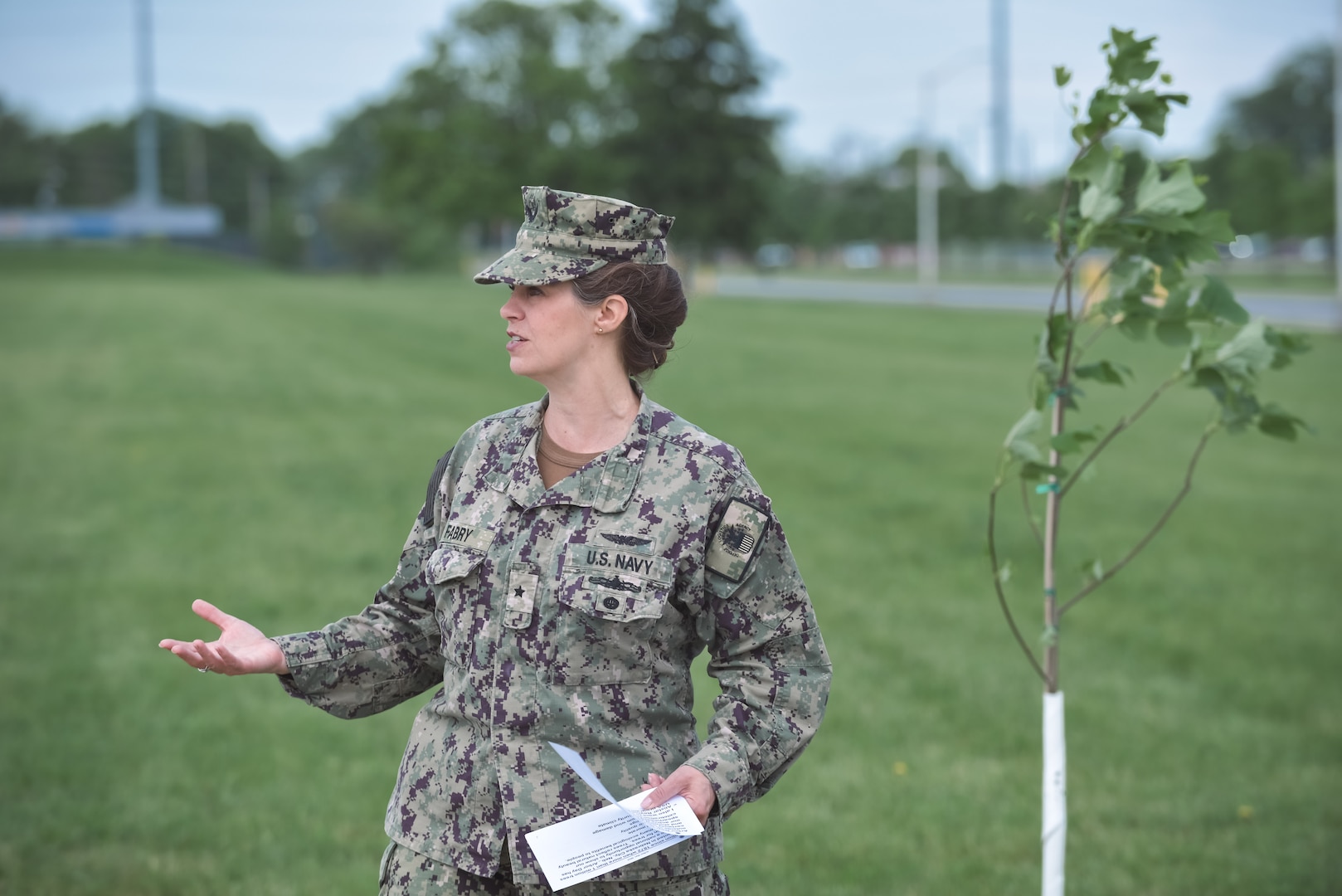 A woman in a military uniform speaks in front of a tulip tree.