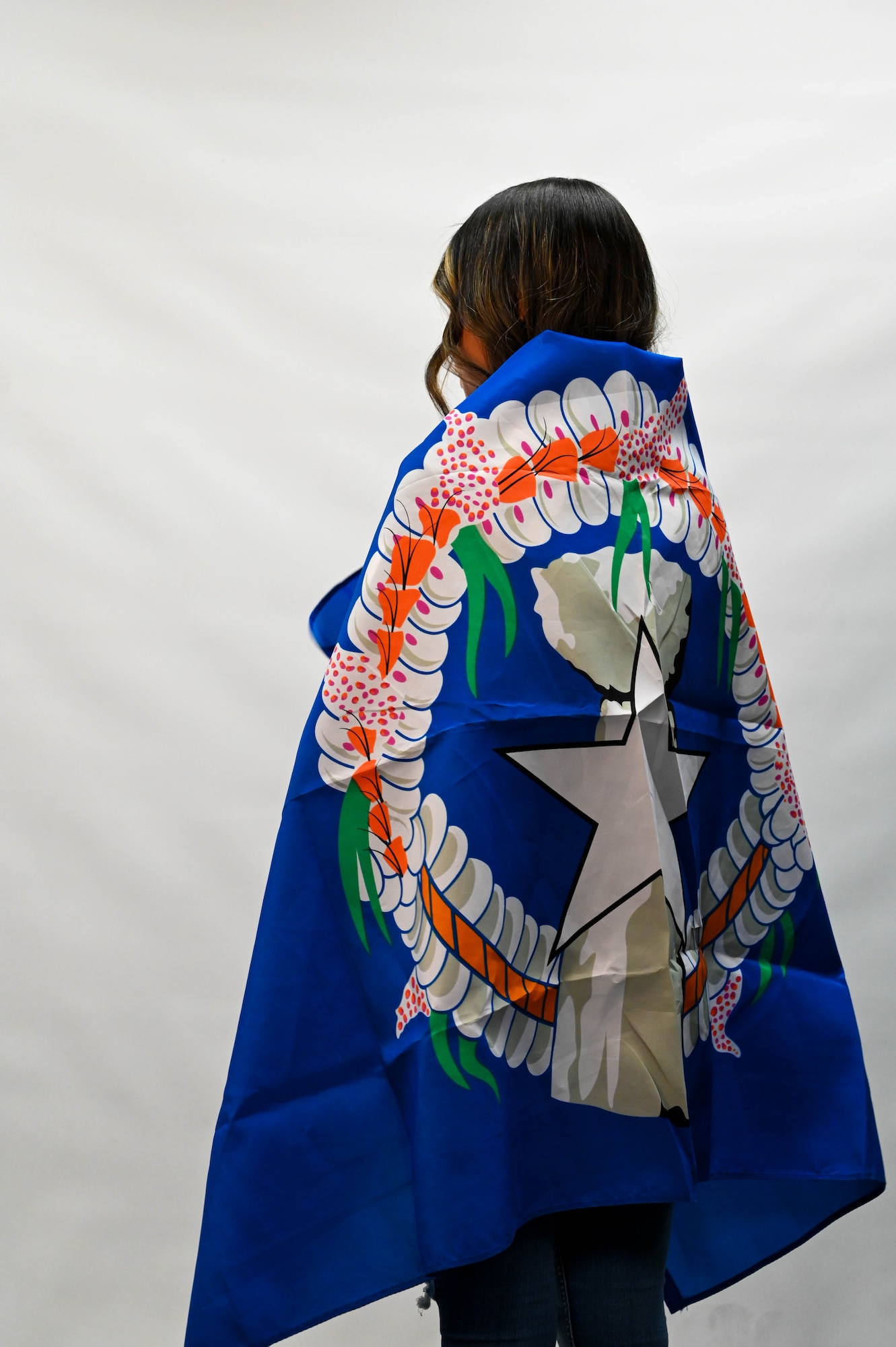 U.S. Air Force Staff Sgt. Margaret Celis, 97th Medical Group pharmacy technician, wraps herself in the flag of the Northern Mariana Islands at Altus Air Force Base, Oklahoma, May 25, 2022. The flag was adopted in 1985 and consists of three symbols: a star representing the United States, a latte stone representing the Chamorros, and a mwarmwar, a decorative wreath representing the Carolinians. The blue background represents the Pacific Ocean and the Mariana Trench. (U.S. Air Force photo by Senior Airman Kayla Christenson)