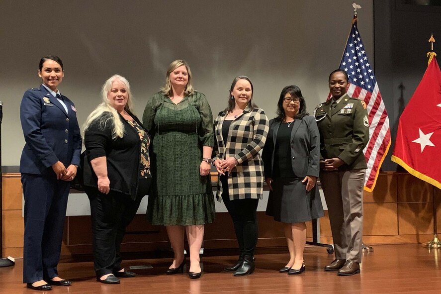 Six people, two in uniform and the others in civilian attire, stand together on a stage.