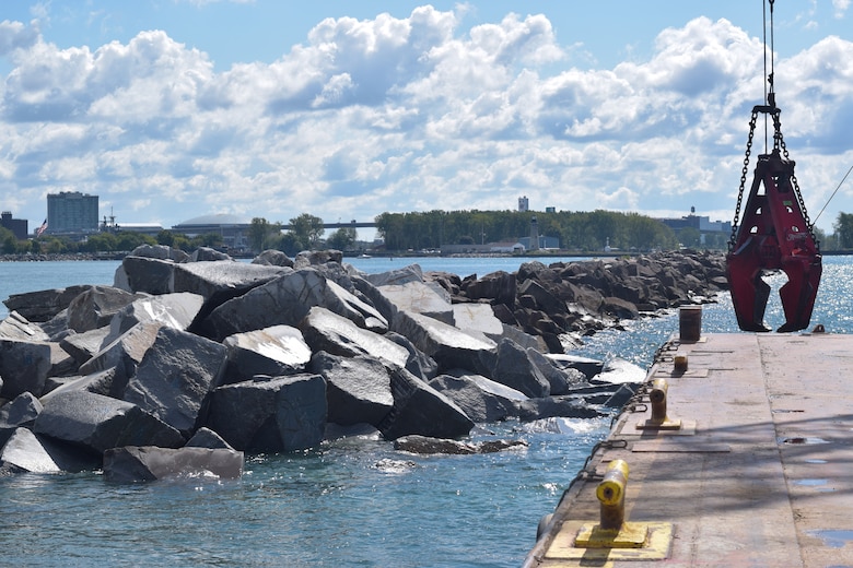 Stone breakwater next to a barge with a claw.