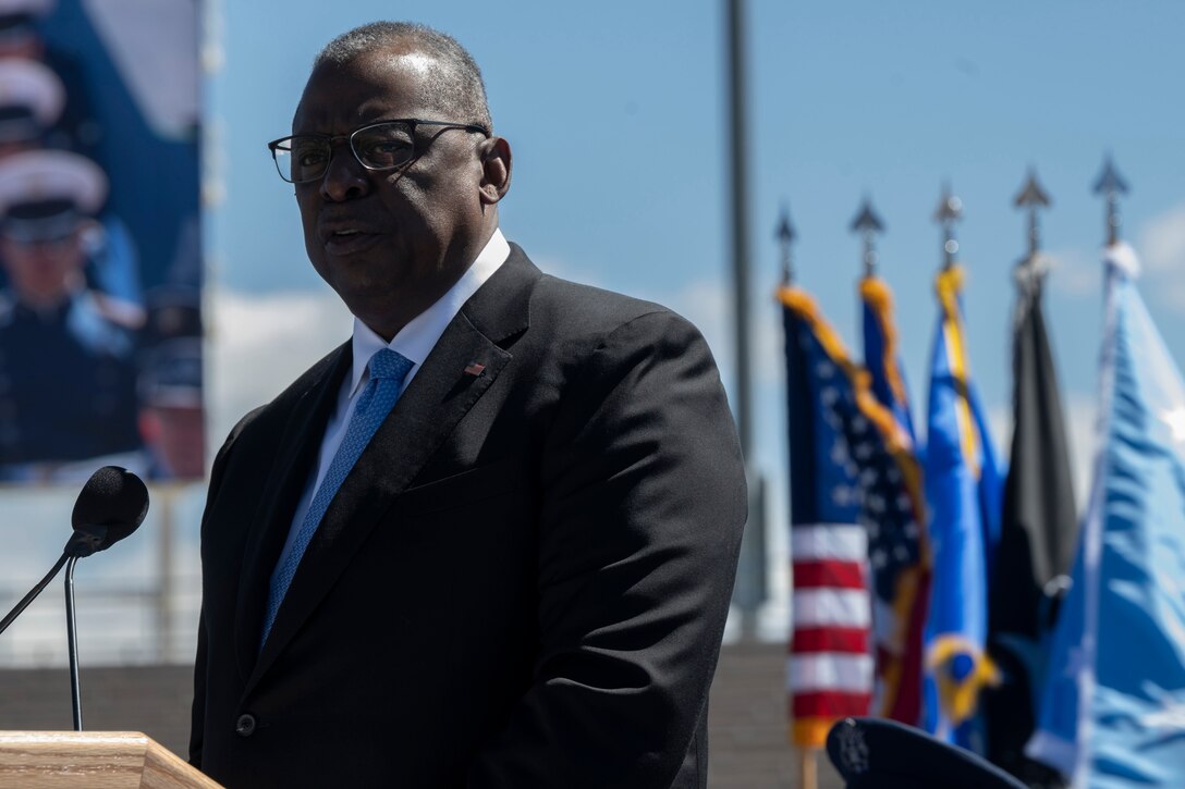 Secretary of Defense Lloyd J. Austin III speaks from a stage with flags behind him.