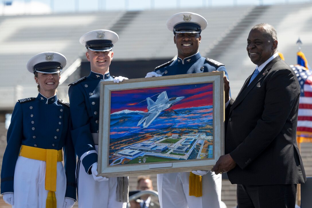 Secretary of Defense Lloyd J. Austin III holds a painting standing with three cadets.