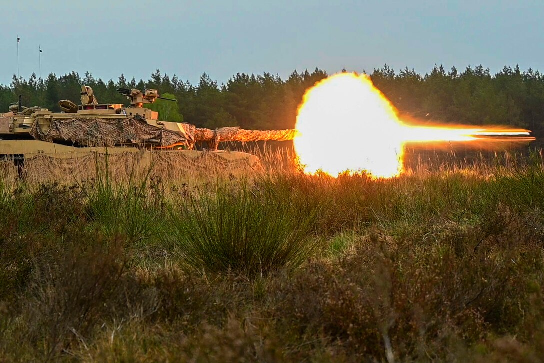 Service members fire ammunition from a tank covered in camouflage material.