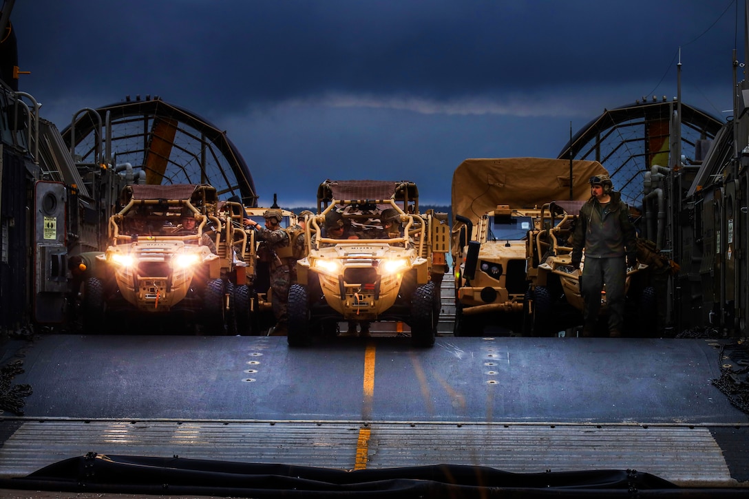 Several service members offload all-terrain vehicles from a landing craft.
