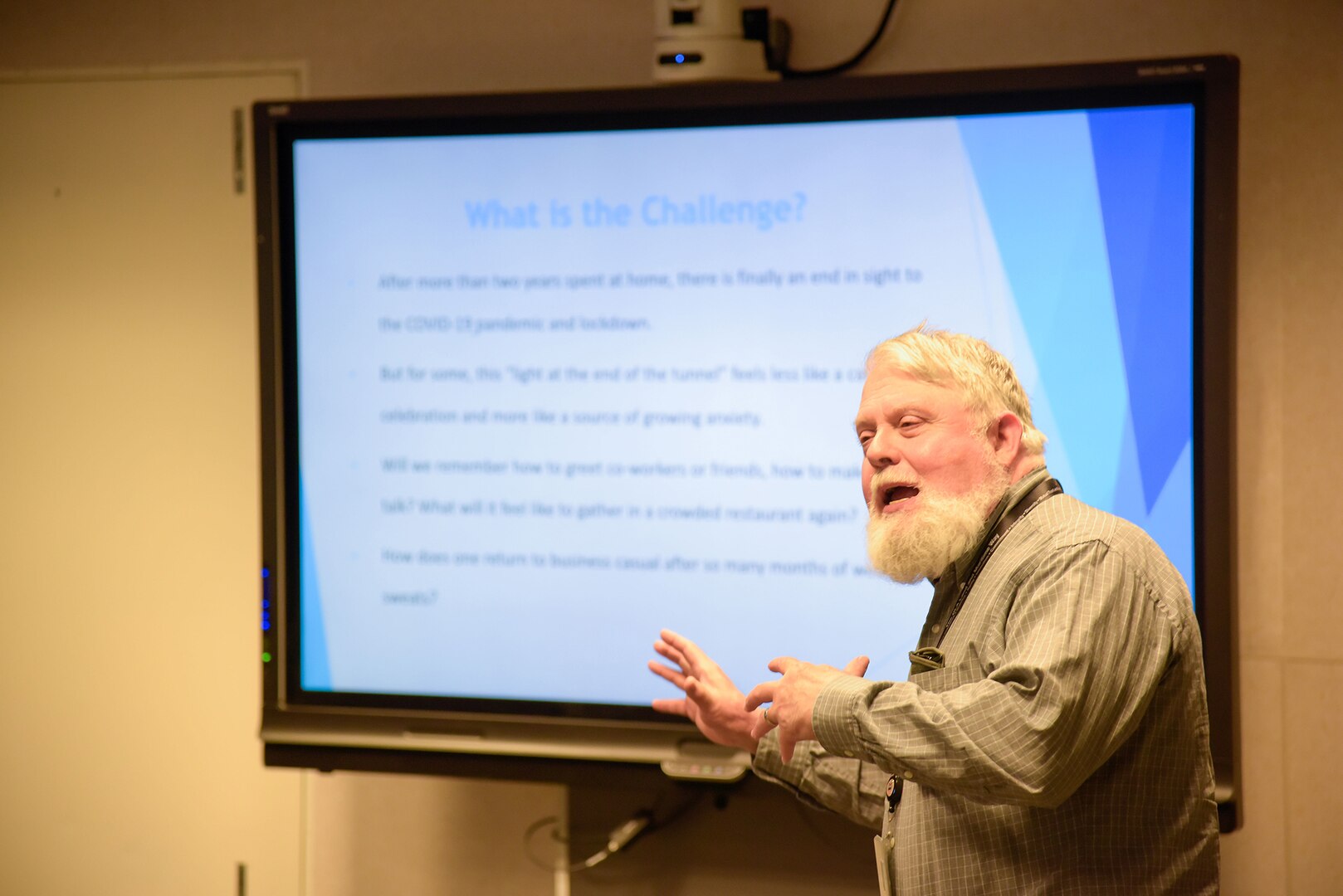 A man with white hair and a beard in front of a Powerpoint presentation.