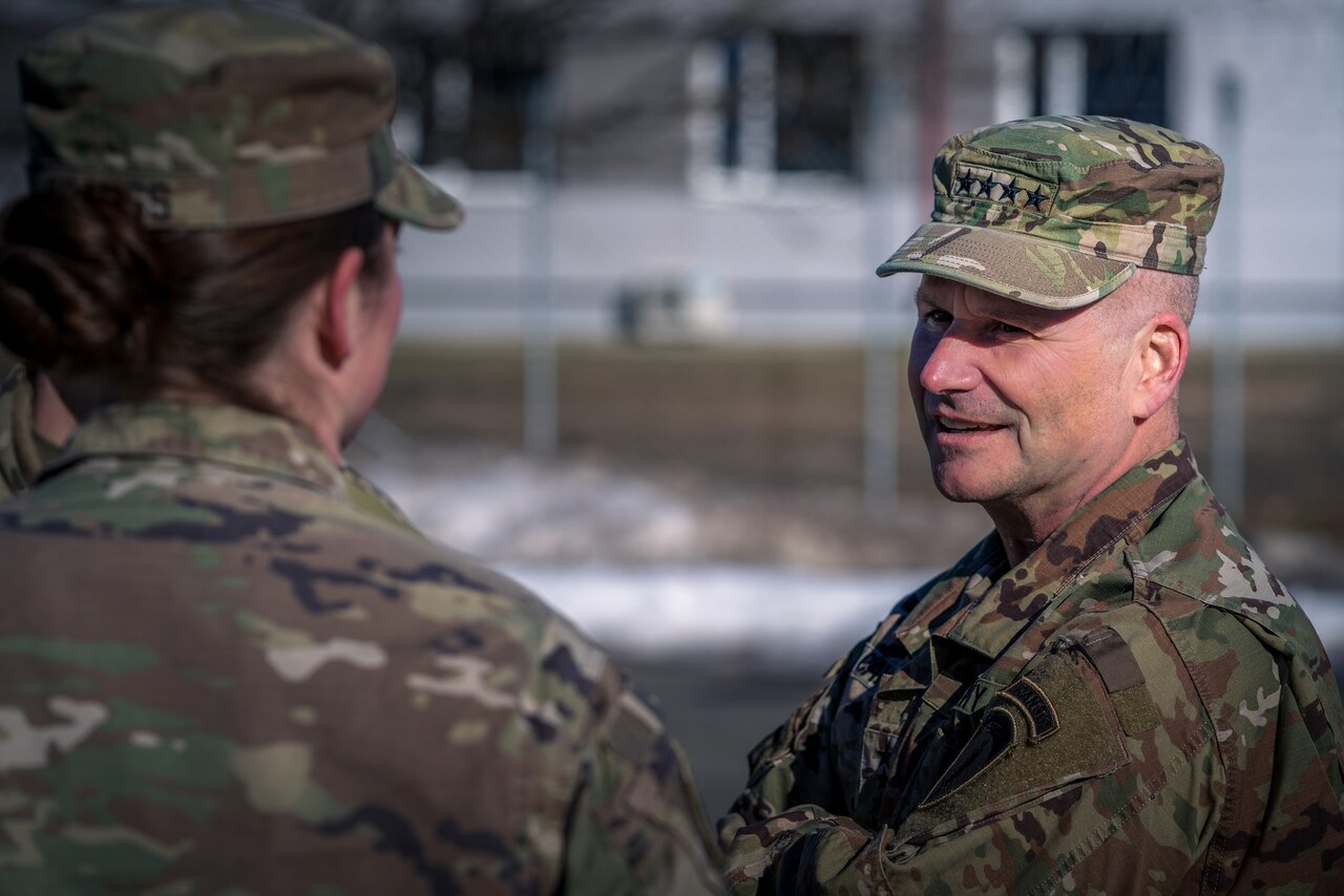 An Army general stands and speaks with a soldier outside.